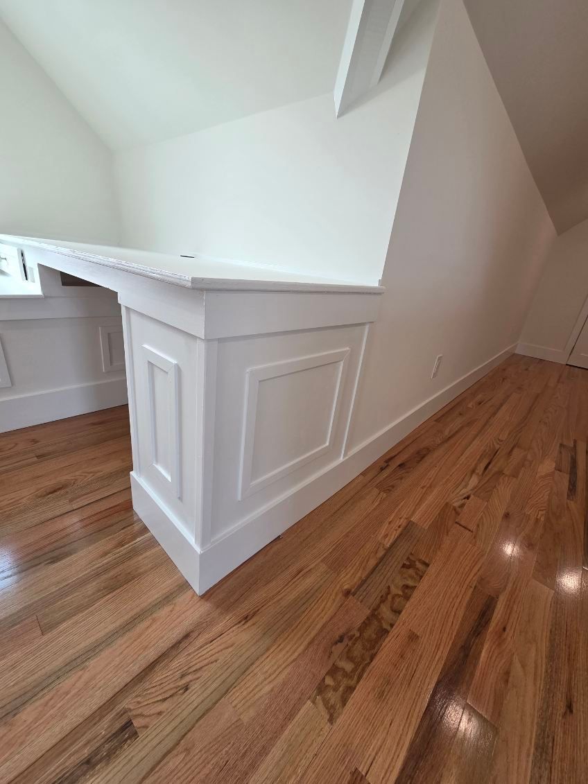 A white paneled custom desk or bar unit with a countertop sits on polished hardwood floors in a corner of a room.