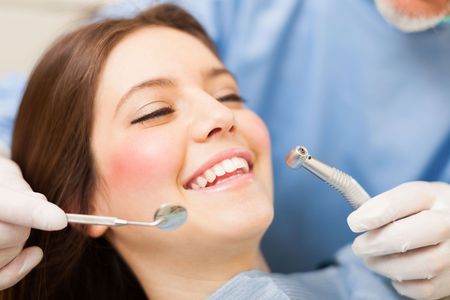 A woman is smiling while having her teeth examined by a dentist.