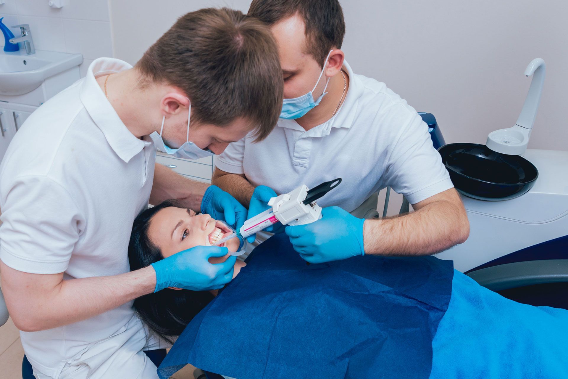 Two dentists are working on a patient 's teeth in a dental office.