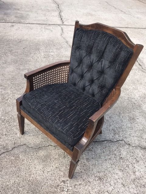 A wooden chair with a black cushion is sitting on a concrete surface.