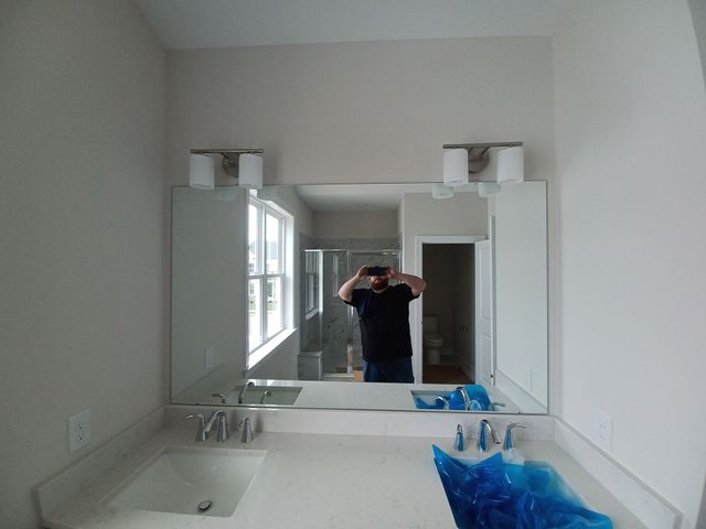 Bathroom vanity with large mirror, sink, and a person taking a mirror selfie in the reflection.