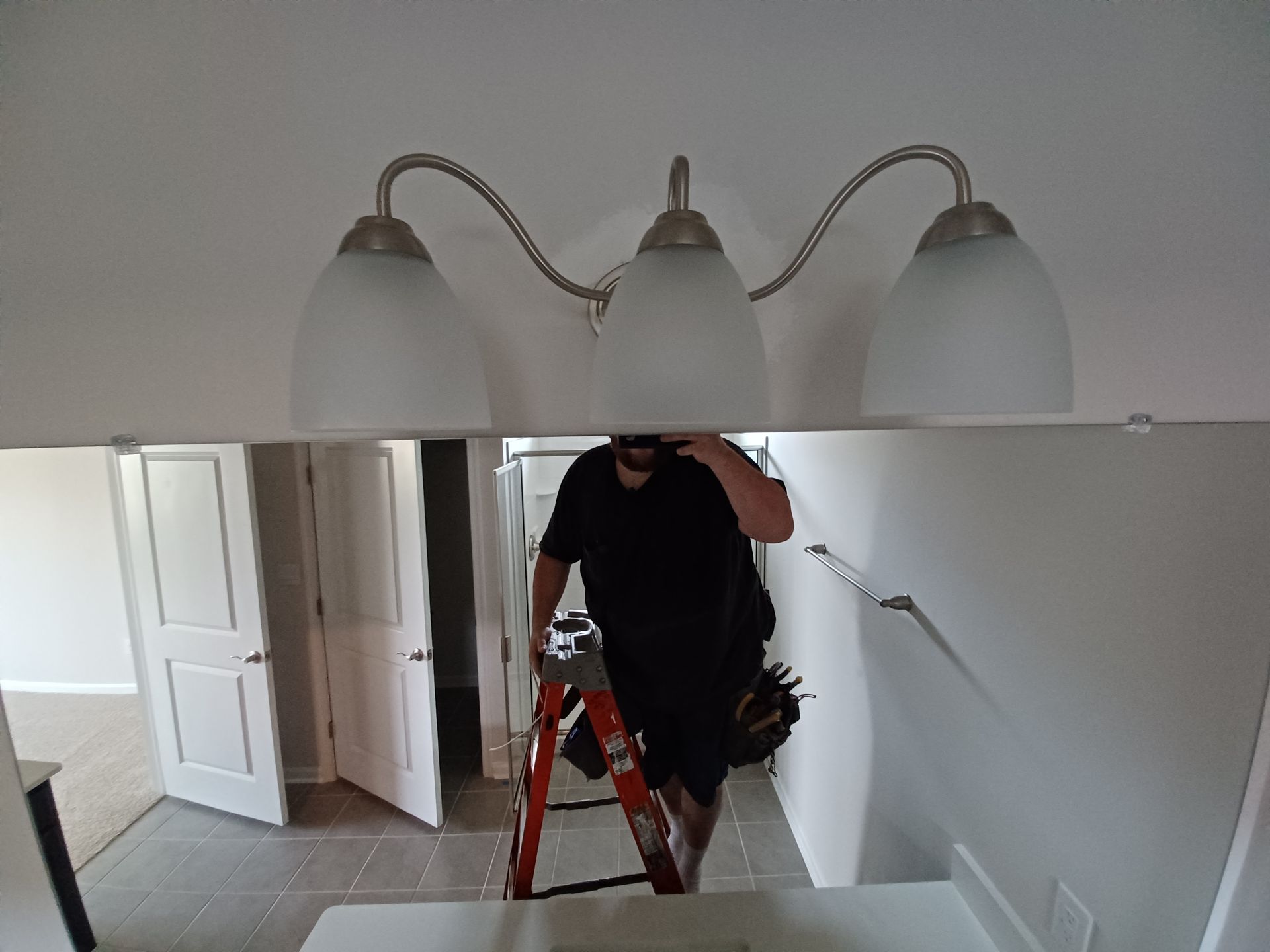 Person on ladder painting a white wall in a room with a mirrored light fixture.