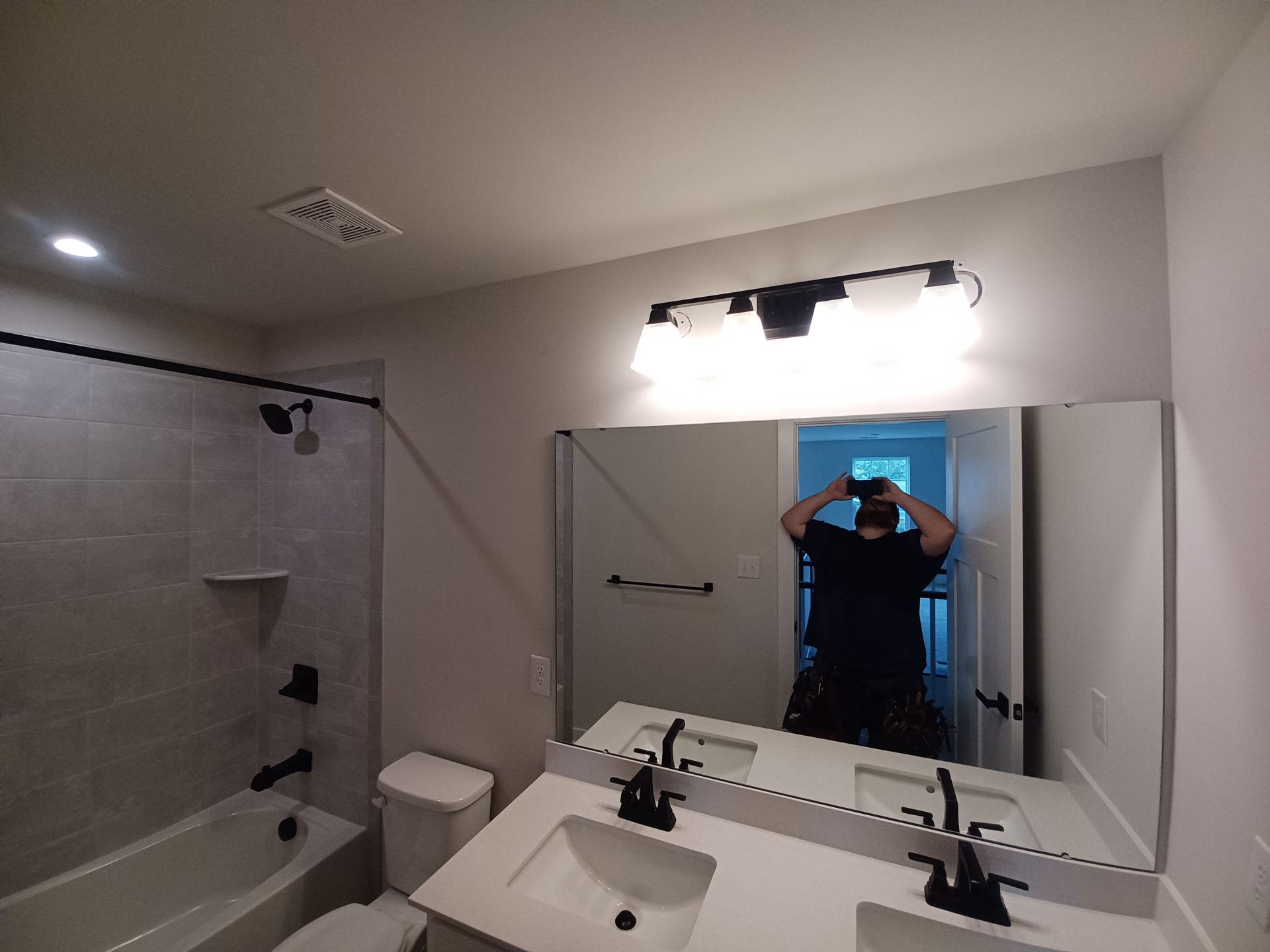 Bathroom with double sink, large mirror, lit vanity, and person taking a mirror selfie.