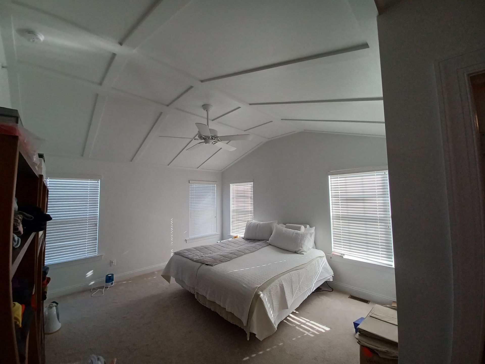 Bright white bedroom with a bed, ceiling fan, and sunlight through window blinds.