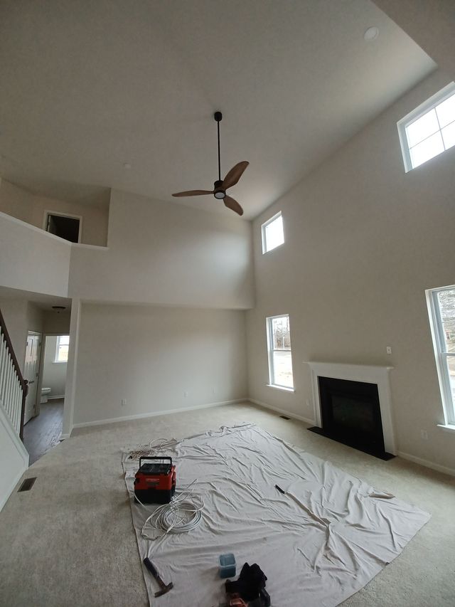 Empty living room under renovation with drop cloths, tools, high ceiling, ceiling fan, and fireplace