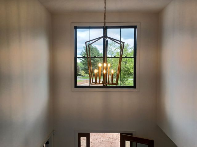 Stairwell with a hanging chandelier and a window overlooking trees and a car outside