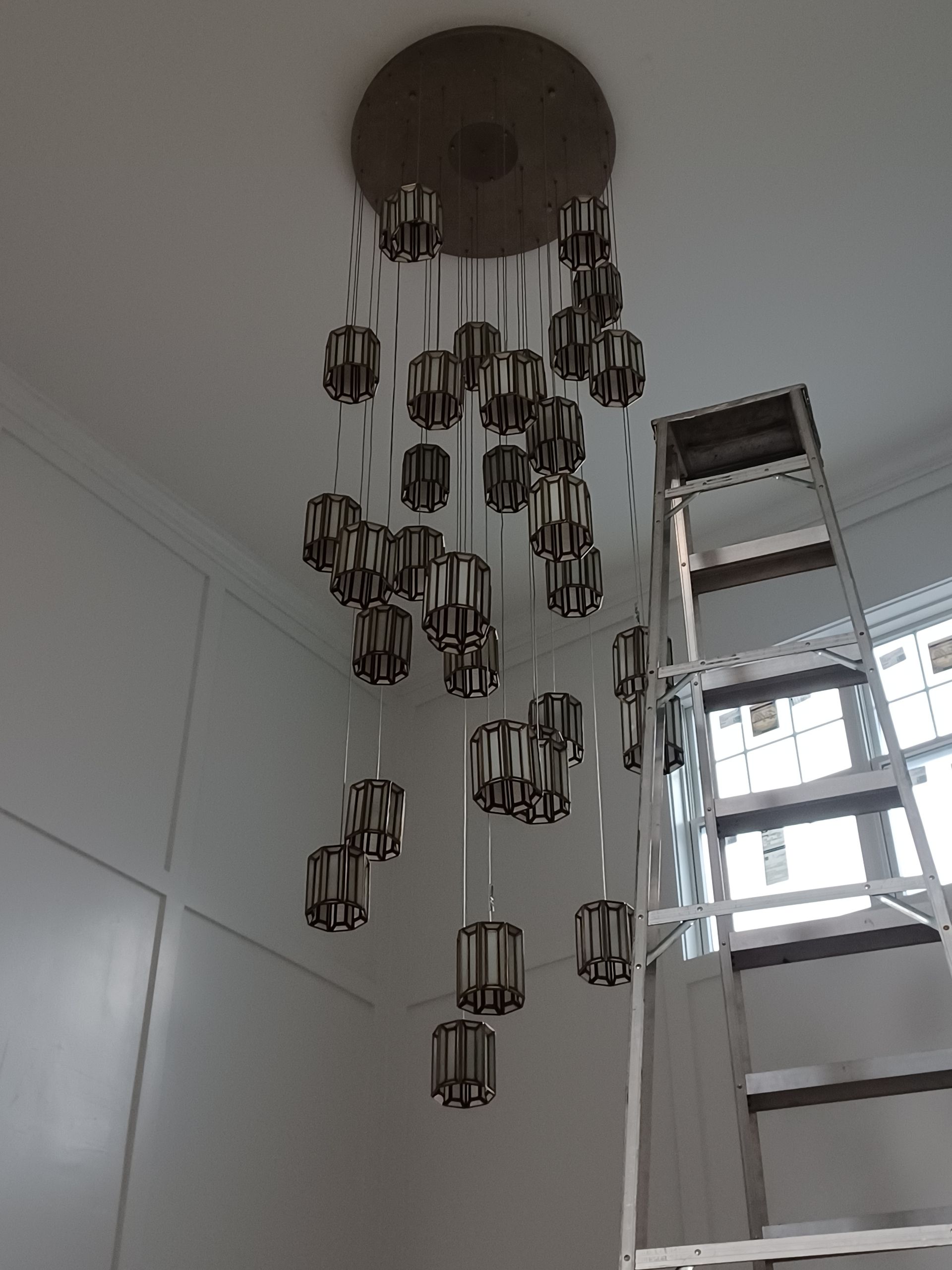 Chandelier with hanging glass pendants in a white room beside a ladder.
