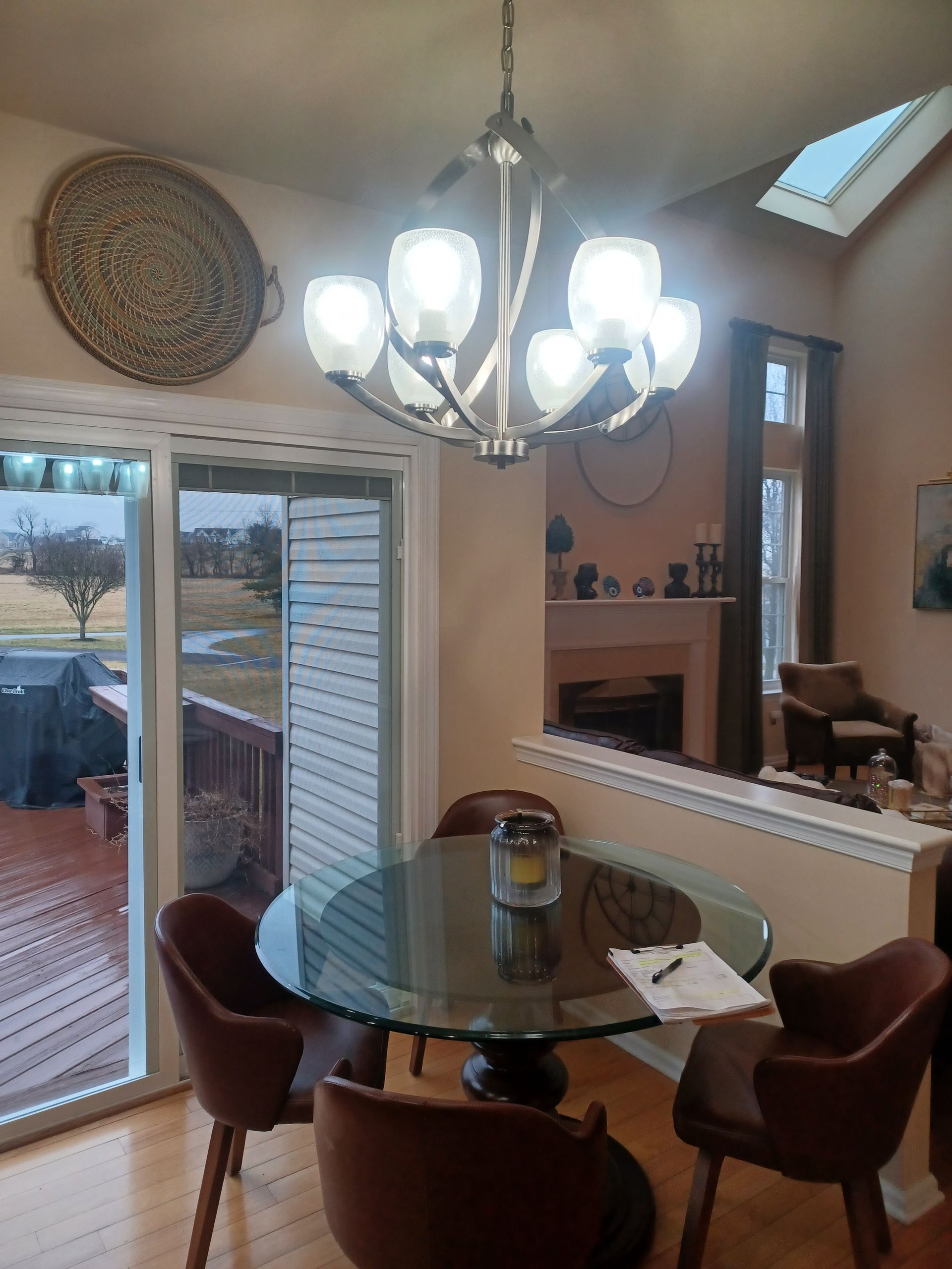 Dining nook with glass table, brown chairs, chandelier, and patio doors overlooking a deck.
