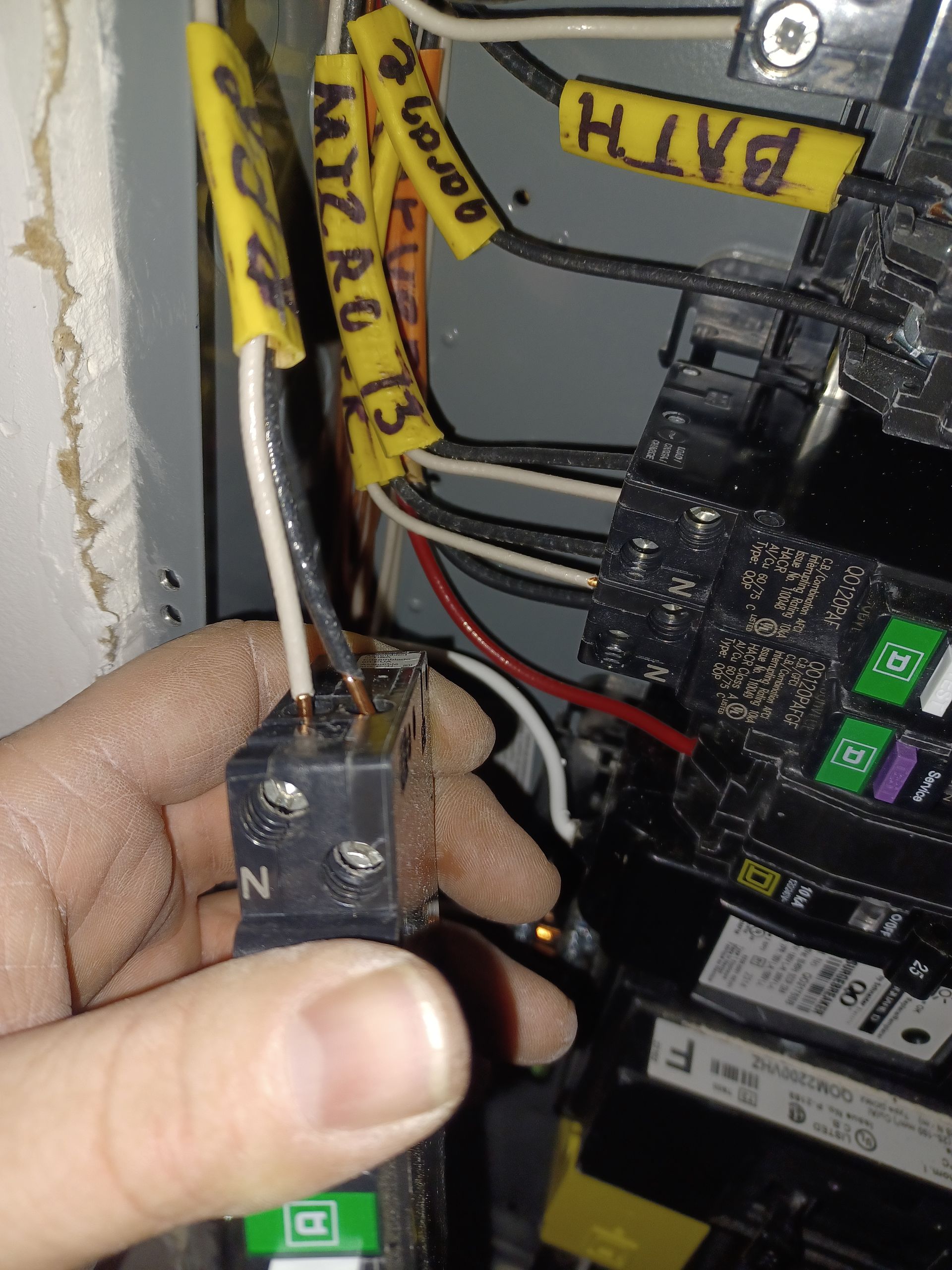 Hand holding a black electrical connector with wires near a circuit board inside a panel.