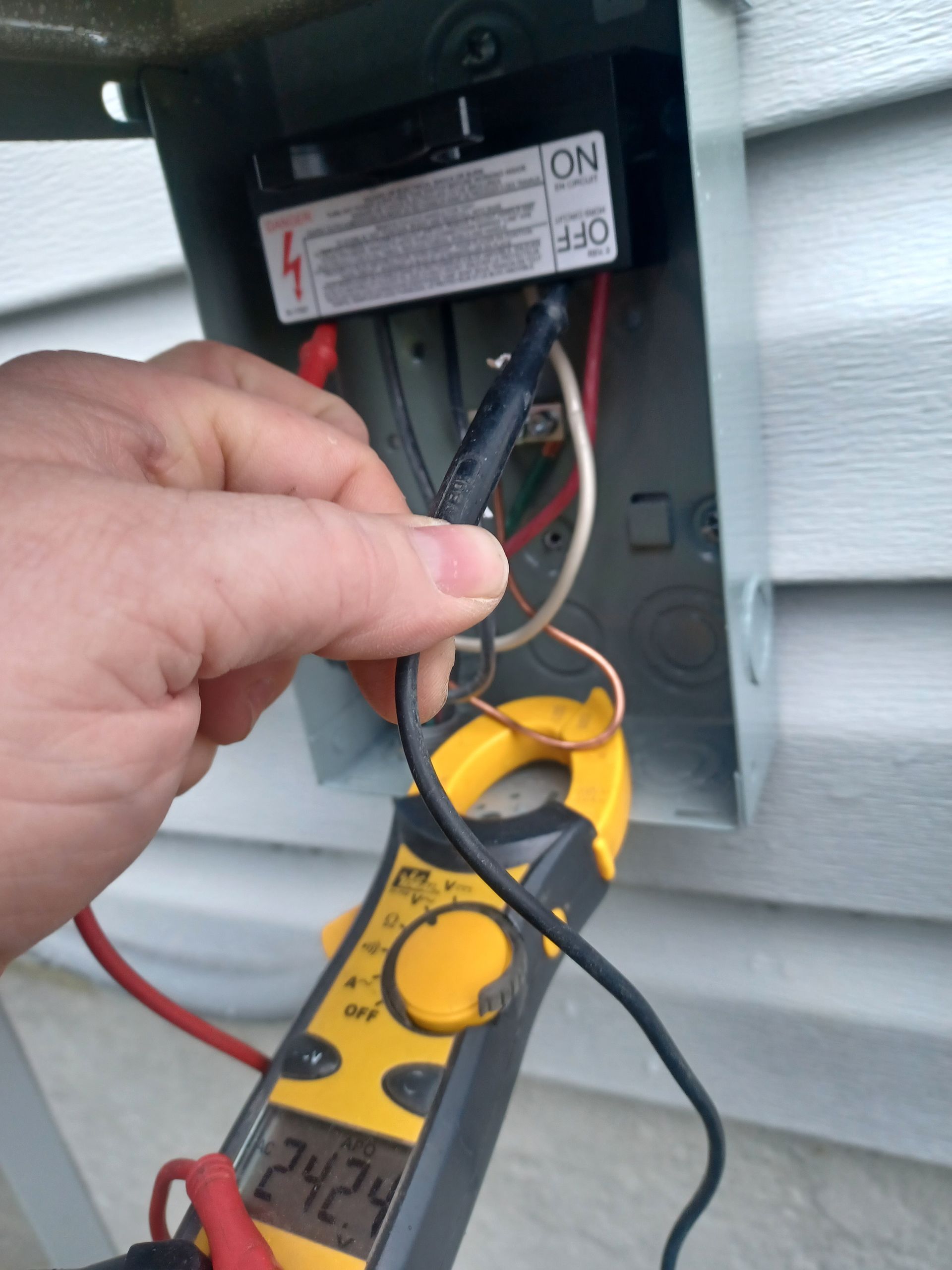 Hand testing wires inside an electrical panel with a yellow multimeter probe connected