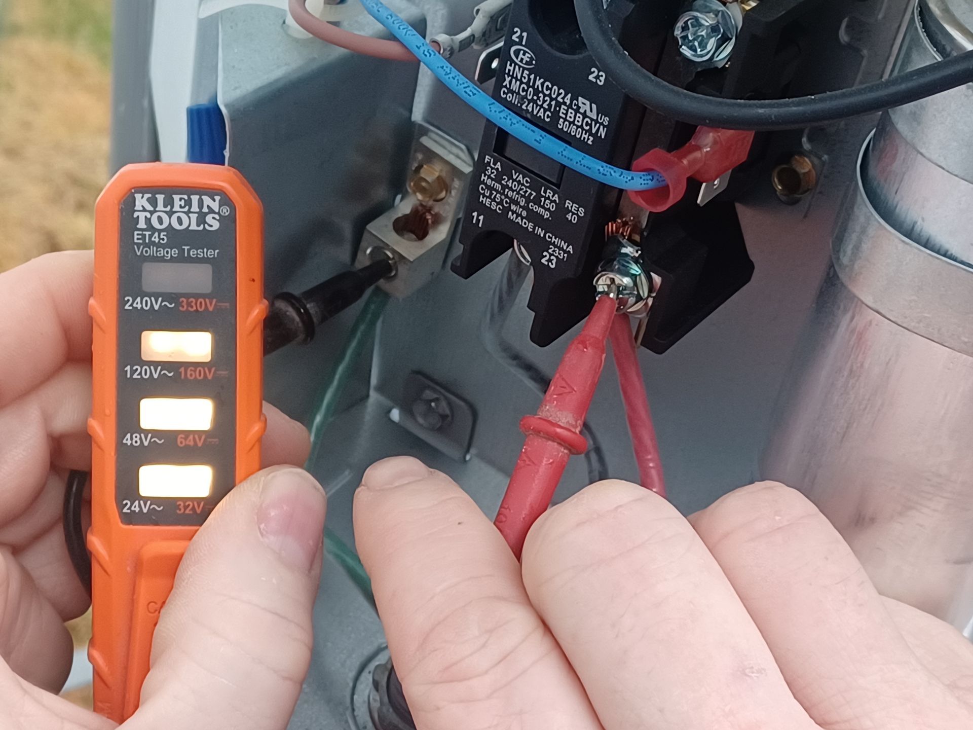 Hand testing electrical wiring with a Klein voltage tester near a metal panel and red wires