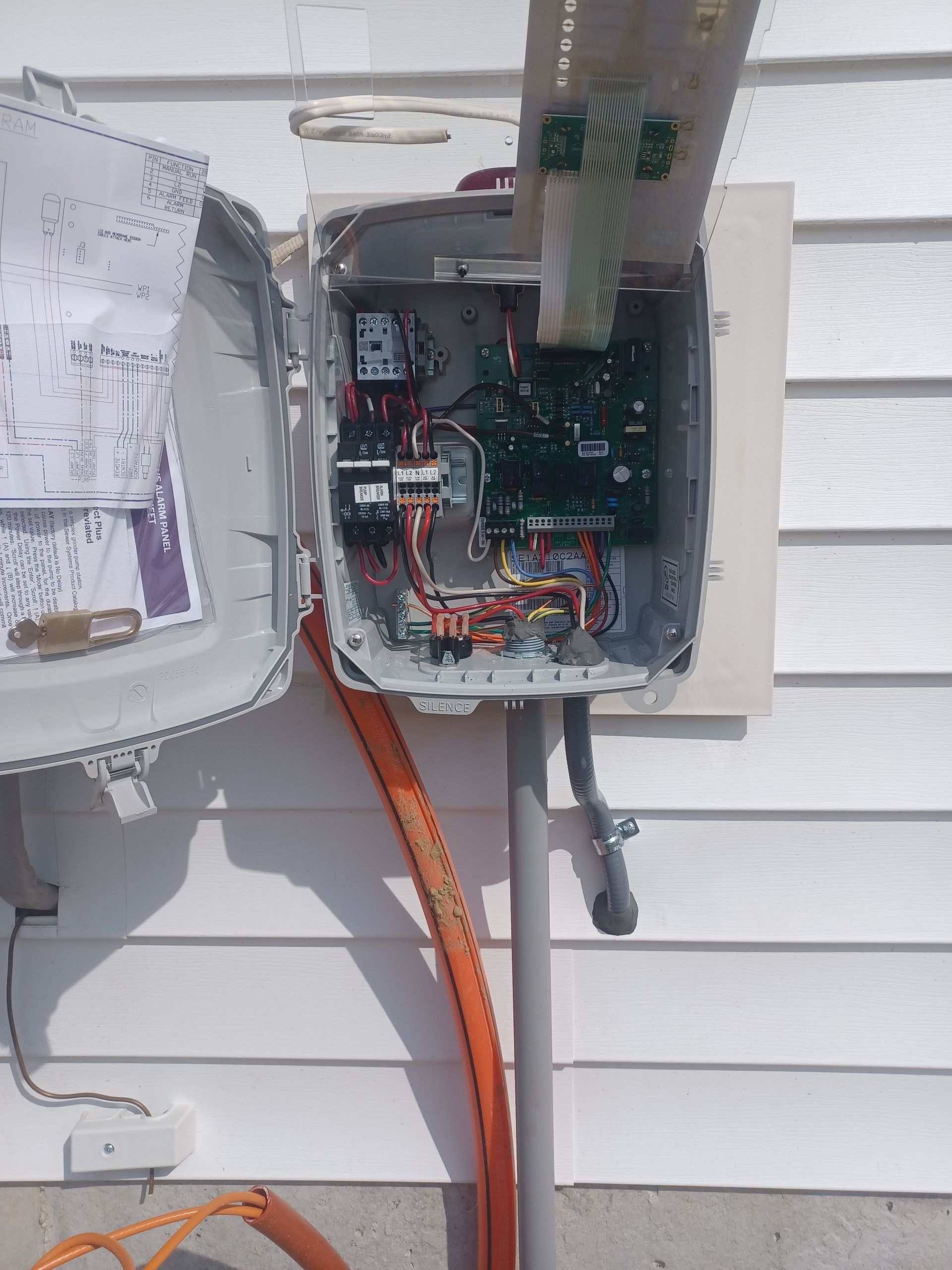 Open electrical breaker panel on white house siding with exposed wiring and orange conduit