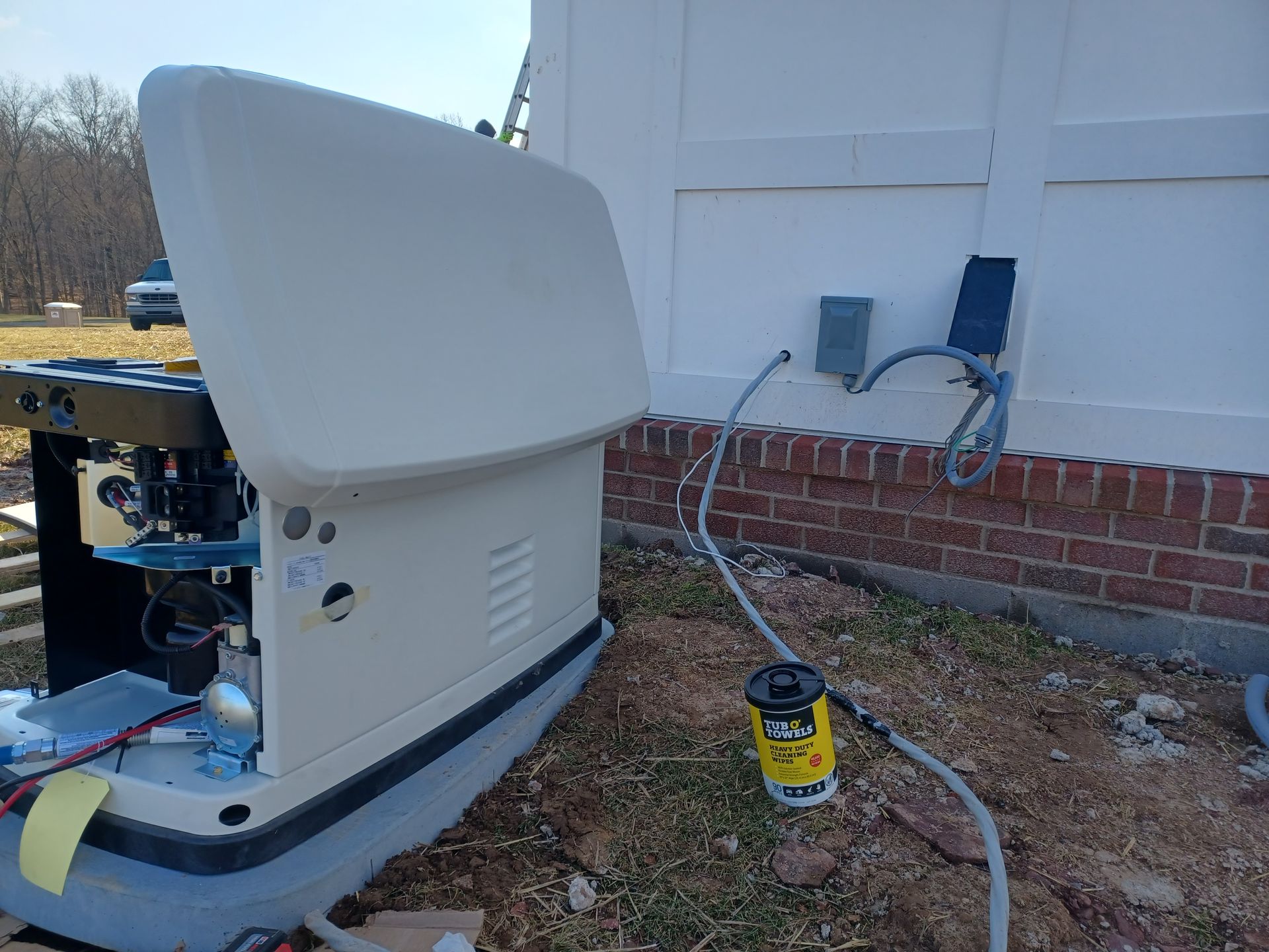 Portable generator on a gravel yard beside a house, with a white cover open and a fuel can nearby.