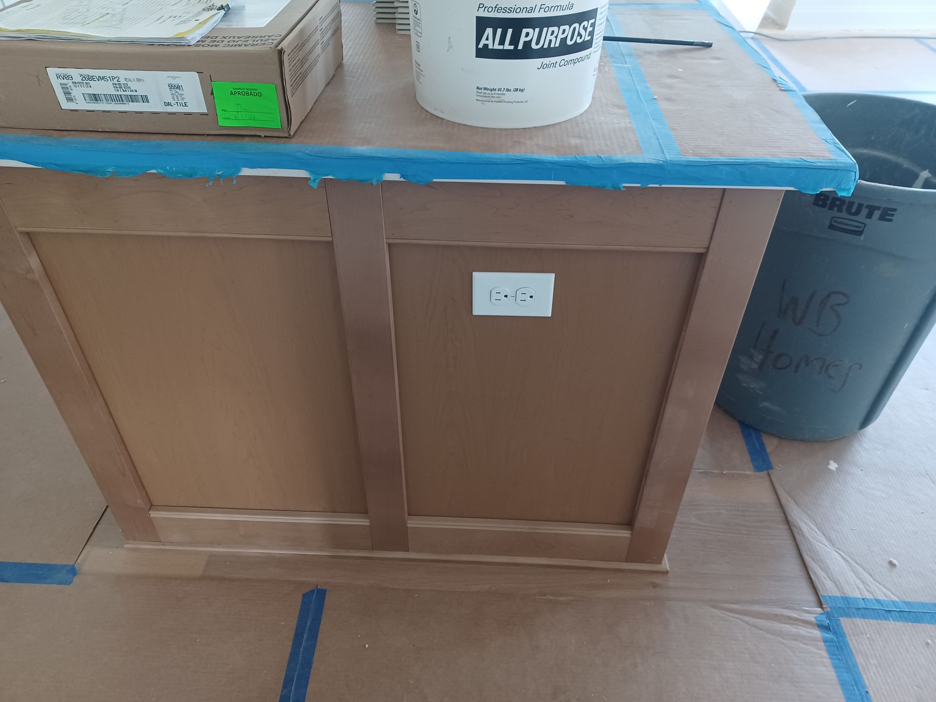 Wooden cabinet with blue-taped top and labeled containers in a workshop or storage area.