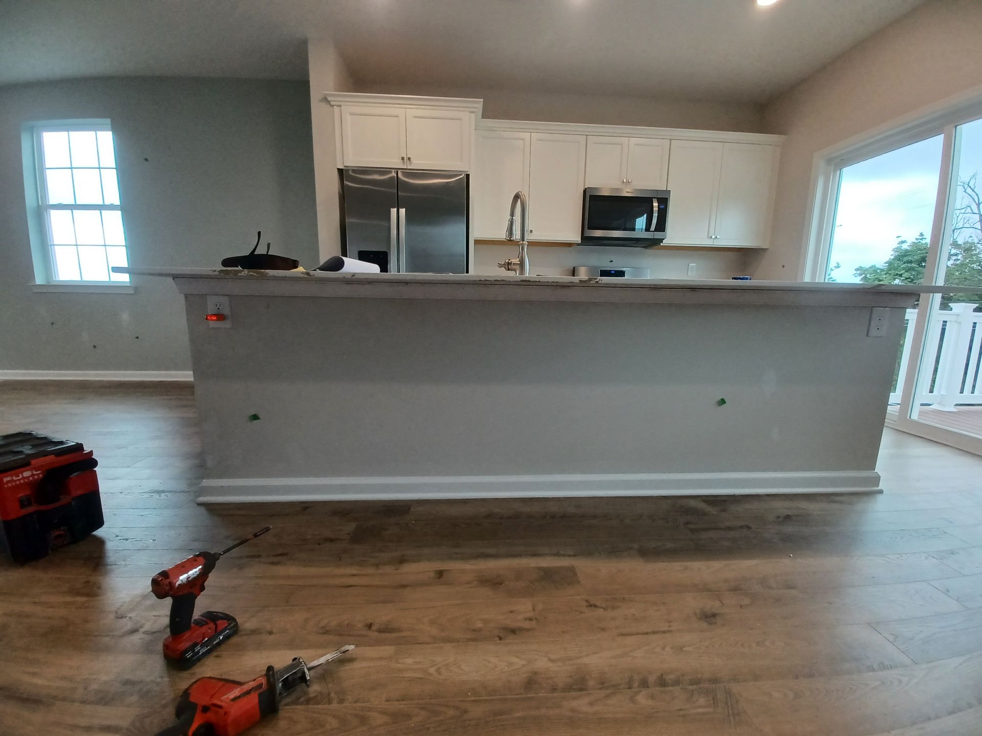 New kitchen with white cabinets, stainless appliances, and hardwood floors; tools lie on the floor in the foreground