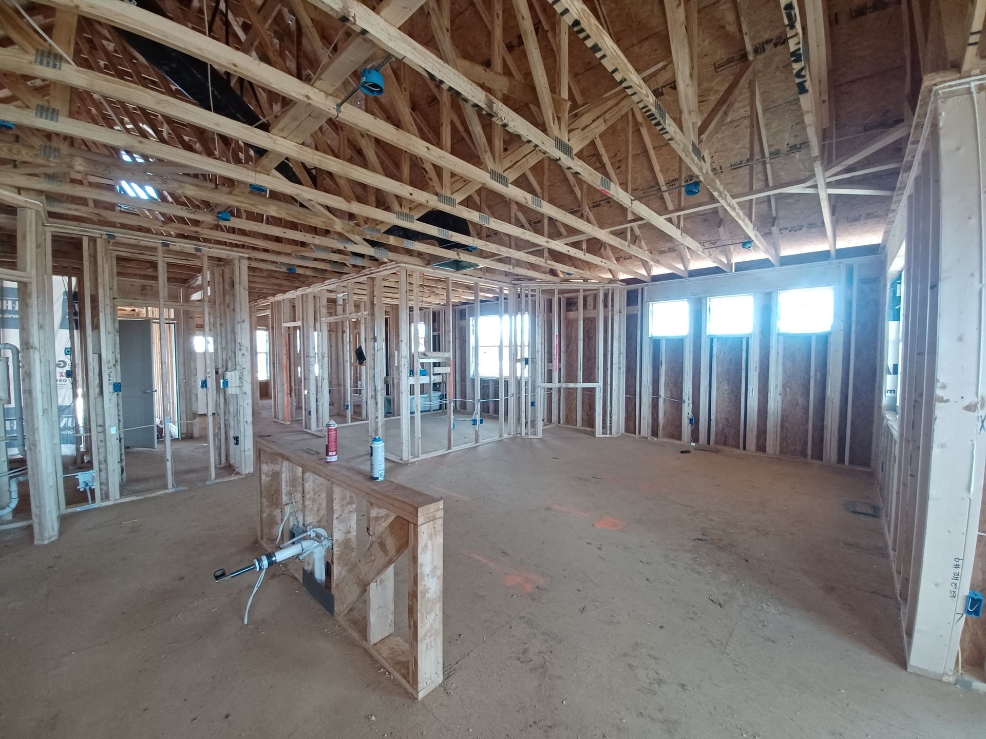 Unfinished house interior with exposed wooden framing, open ceiling joists, and construction tools on the dirt floor