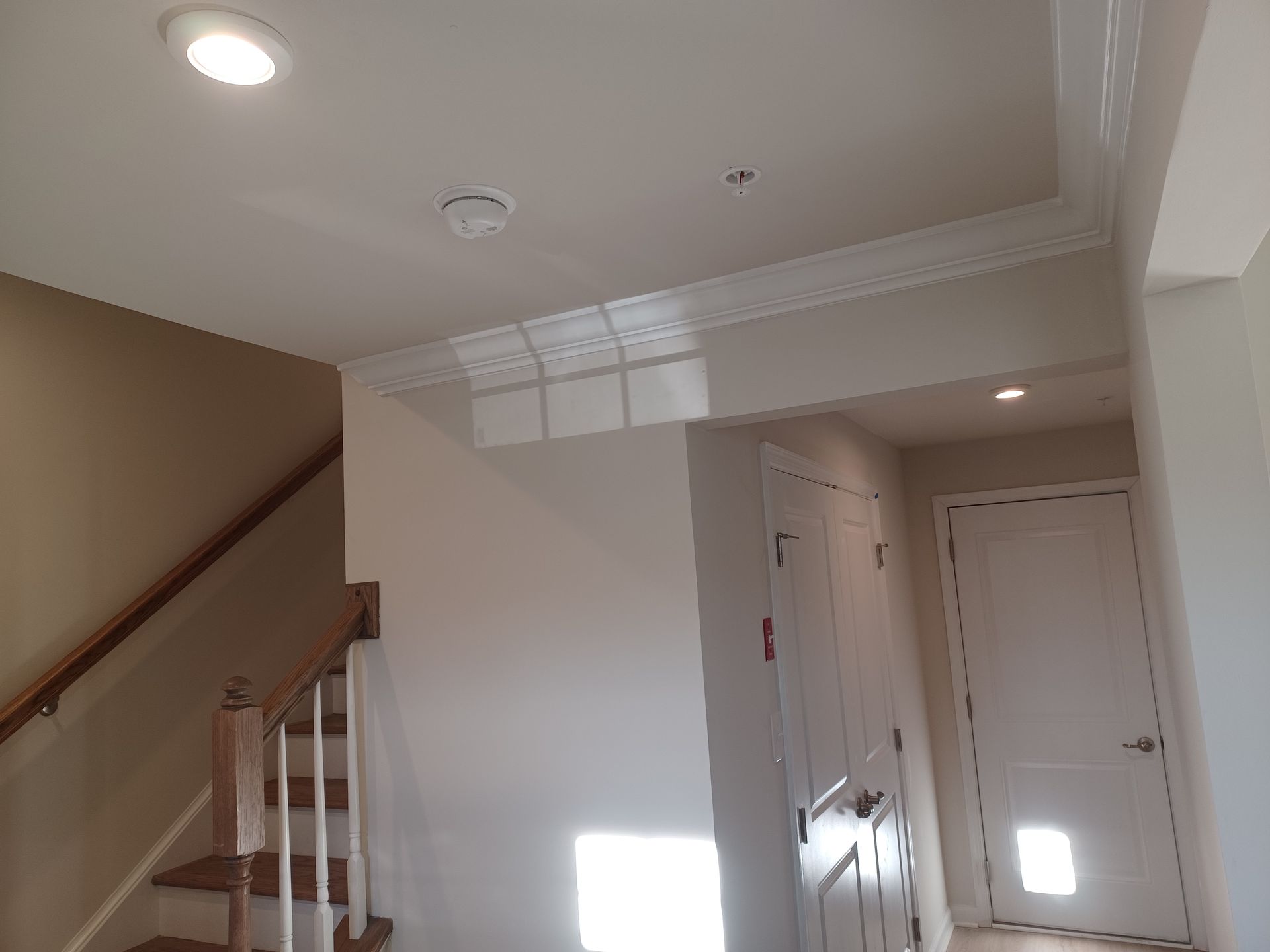 Indoor entryway with stairs, white doors, and a bright sunlit patch on the wall