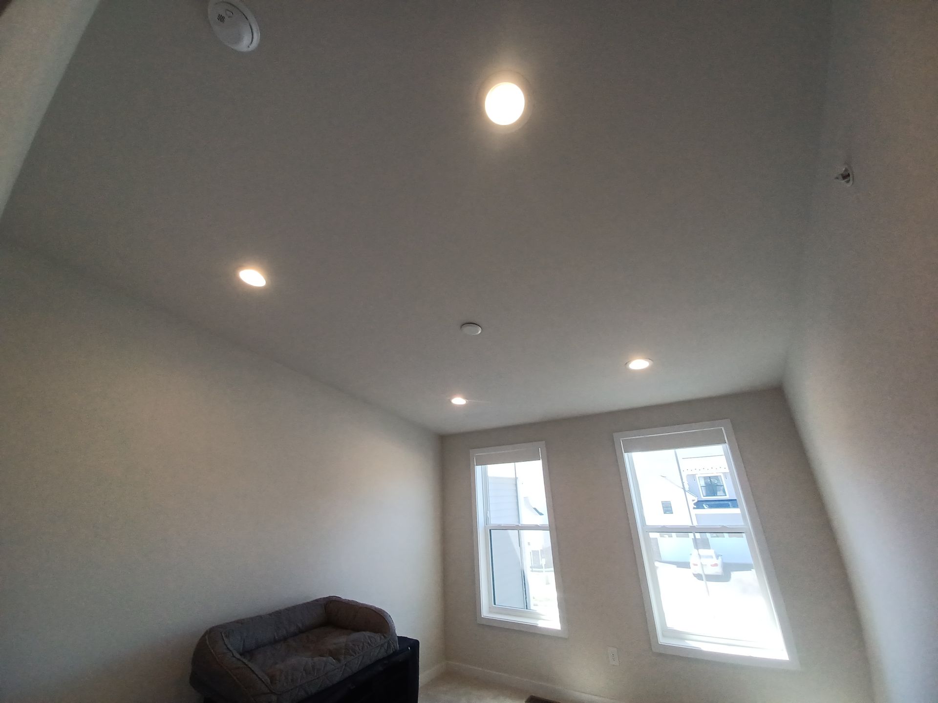 Empty white room with recessed ceiling lights, a dark sofa, and two windows.
