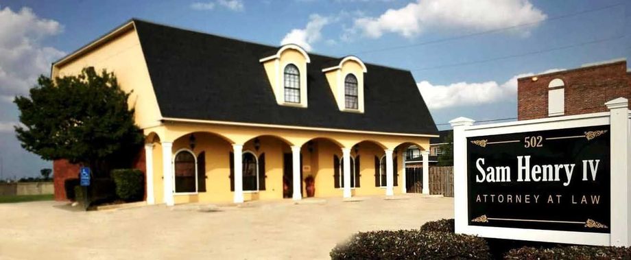 Exterior view of Sam Henry IV Attorney at Law office. The yellow building has a black roof and a sign in the foreground.