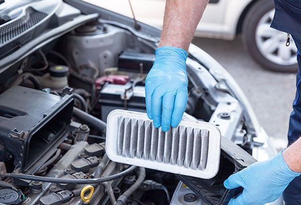 A man wearing blue gloves is cleaning the air filter of a car.