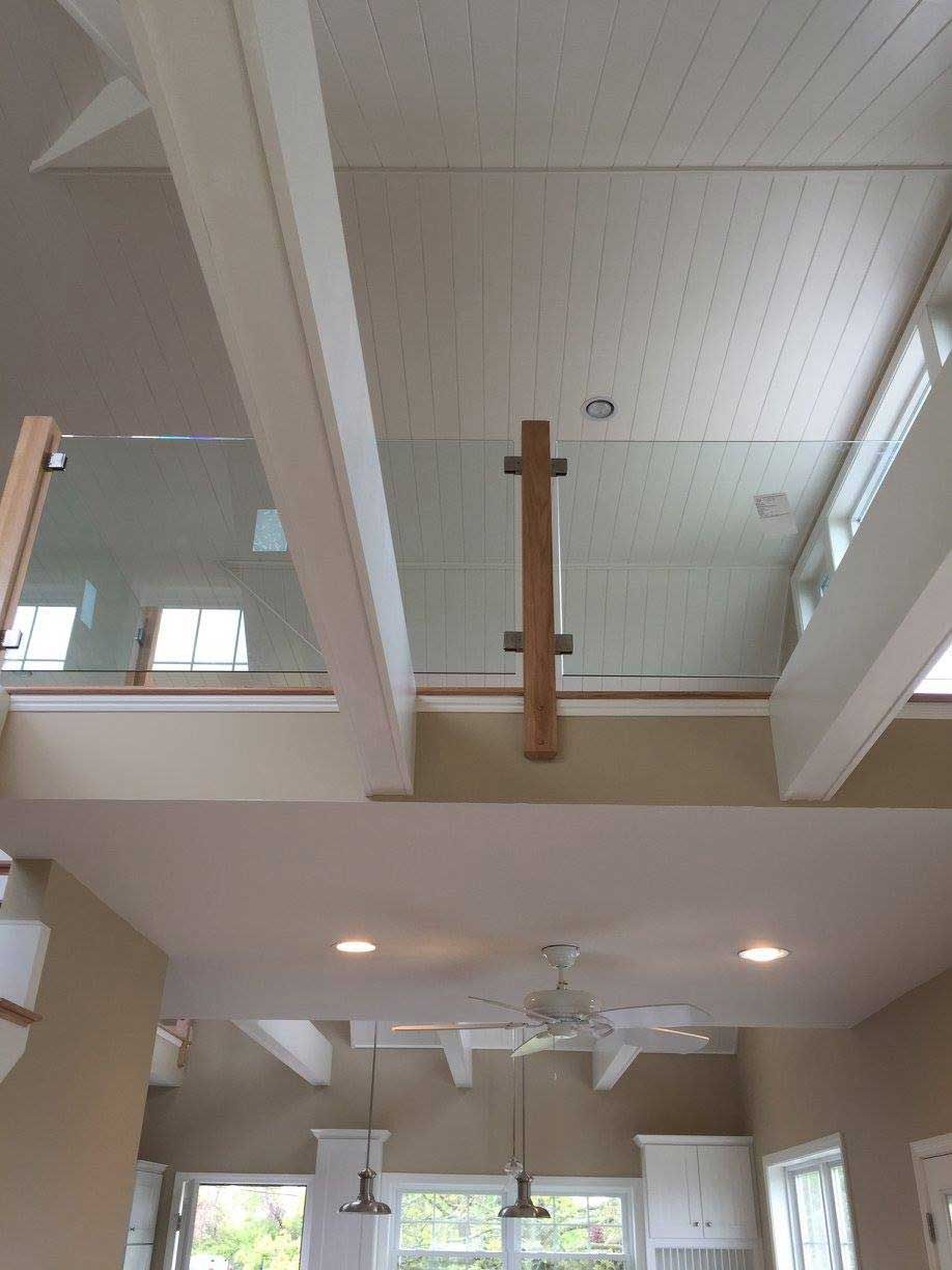 Interior view of a two-story home with glass railing, white beams, and a light-colored wood ceiling.