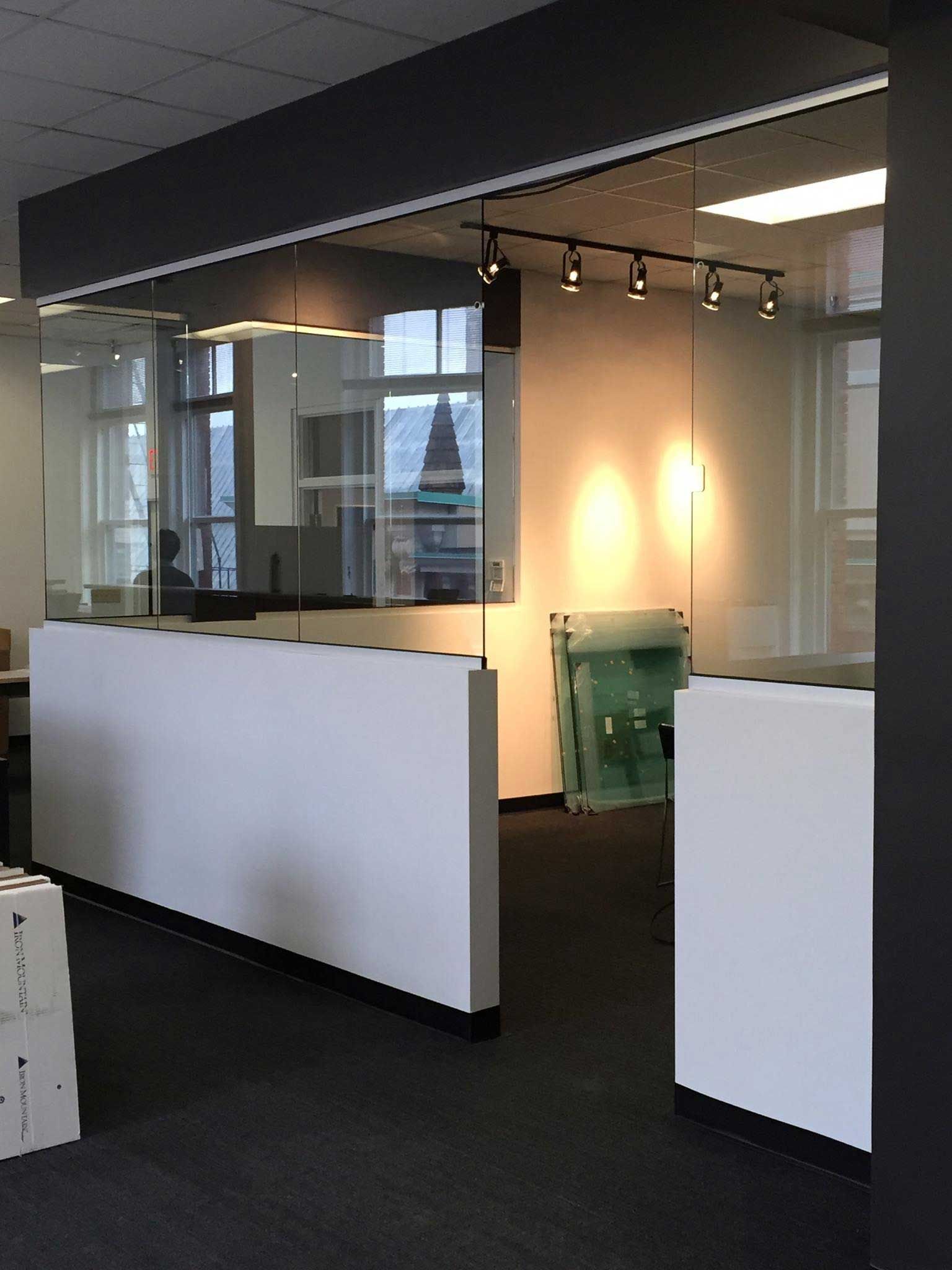 Modern office space with white walls, glass partitions, and track lighting.