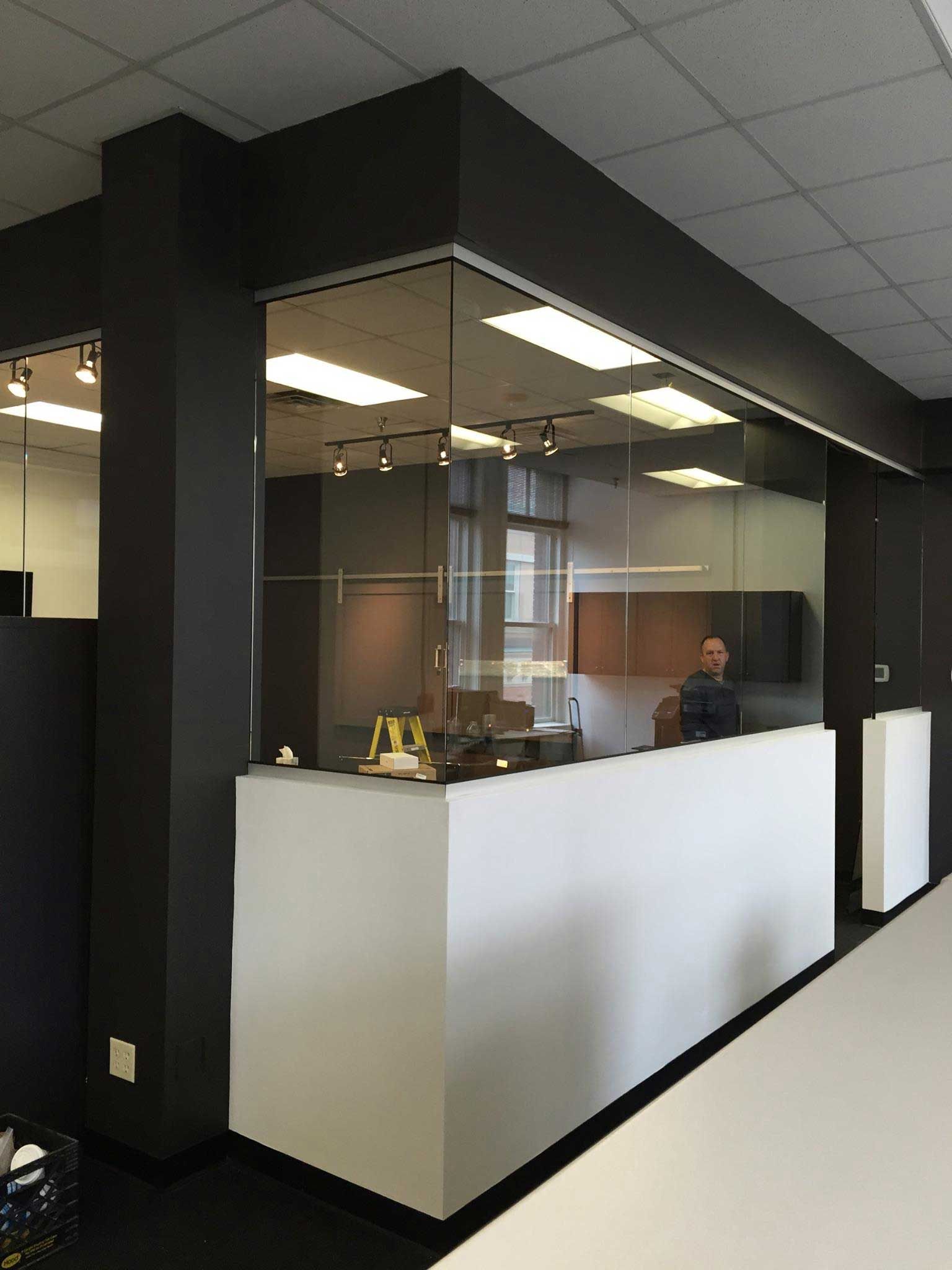 Modern office reception area with white desk, glass wall, and person standing behind it. Black accents.