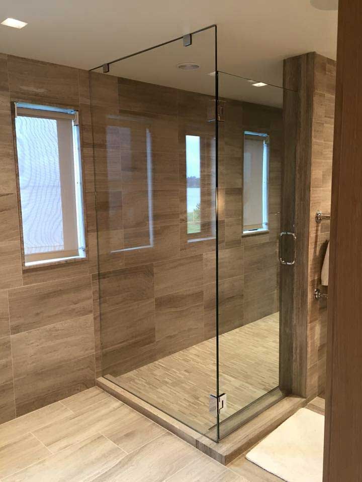 Glass shower enclosure in a tiled bathroom with three windows.