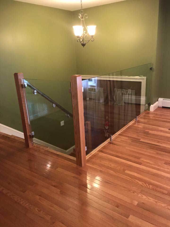 Glass and wood railing at top of stairs in a room with hardwood floors and olive-green walls.