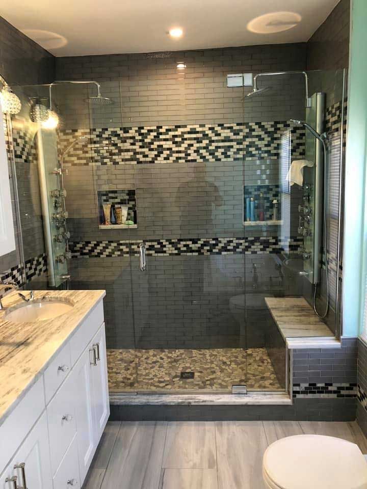 Modern bathroom with gray tile shower, glass doors, built-in bench, and white vanity.