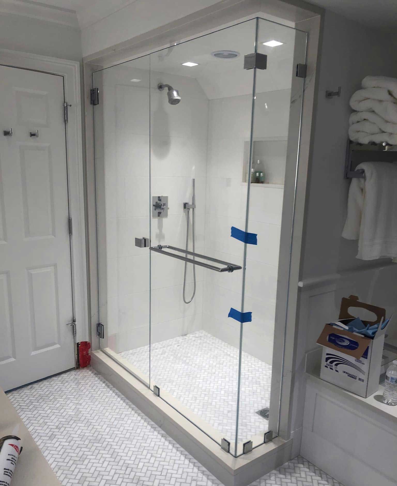 Glass shower enclosure with white tiled interior, chrome fixtures, and a glass door.