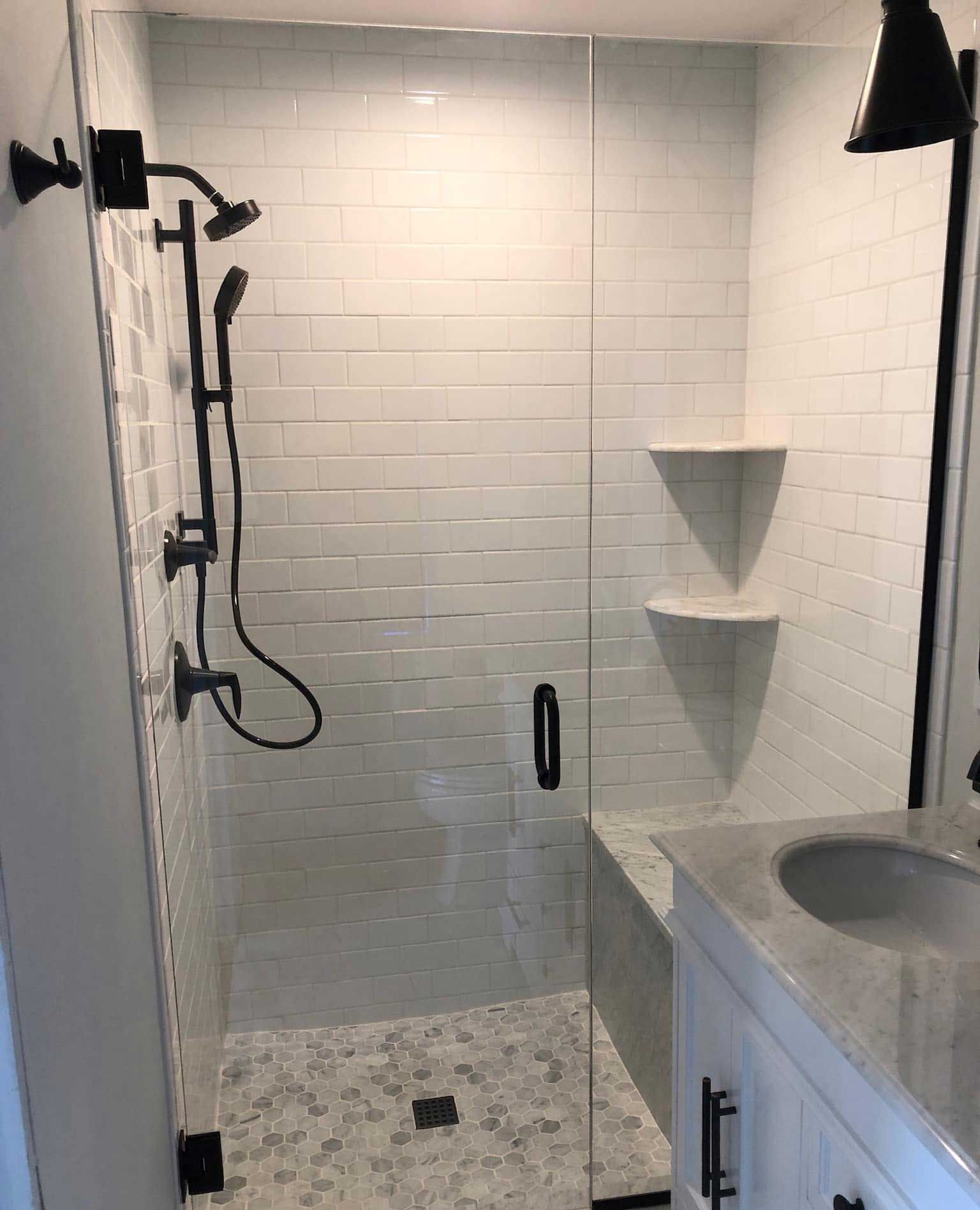 Bathroom with glass shower door, white tiled walls, black shower fixtures, and a vanity.