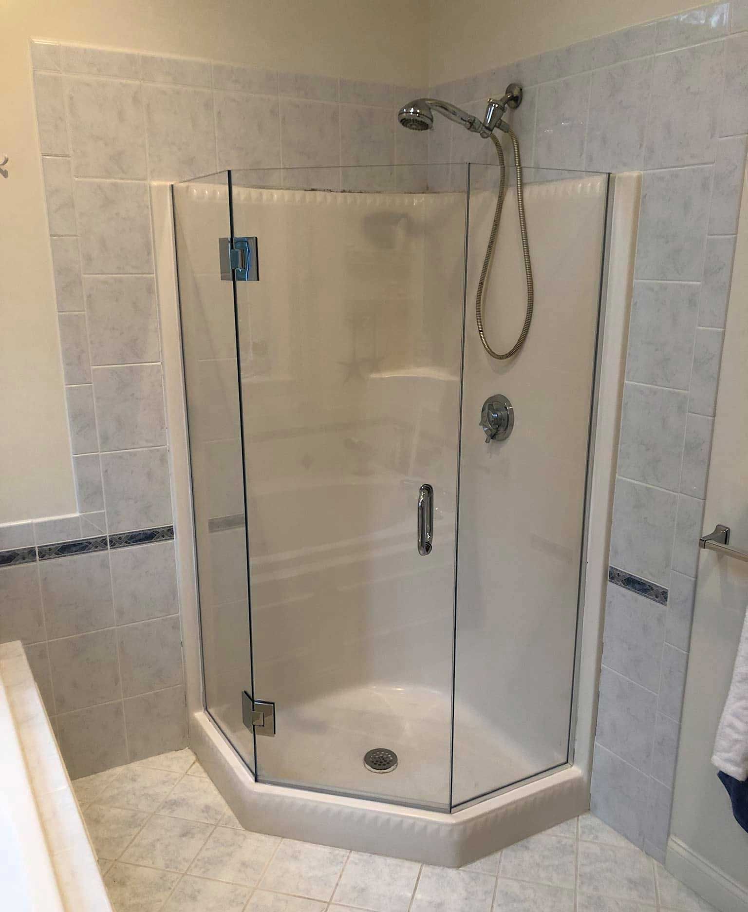 Corner shower with glass doors, white walls, and silver showerhead, tile surround, bathroom.