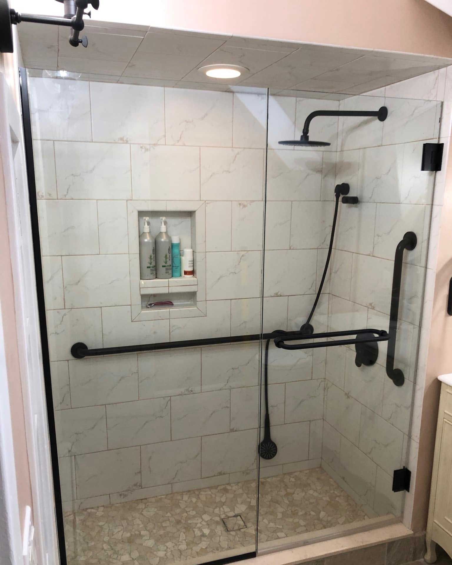 Accessible glass shower with black fixtures and grab bars. White tile background.