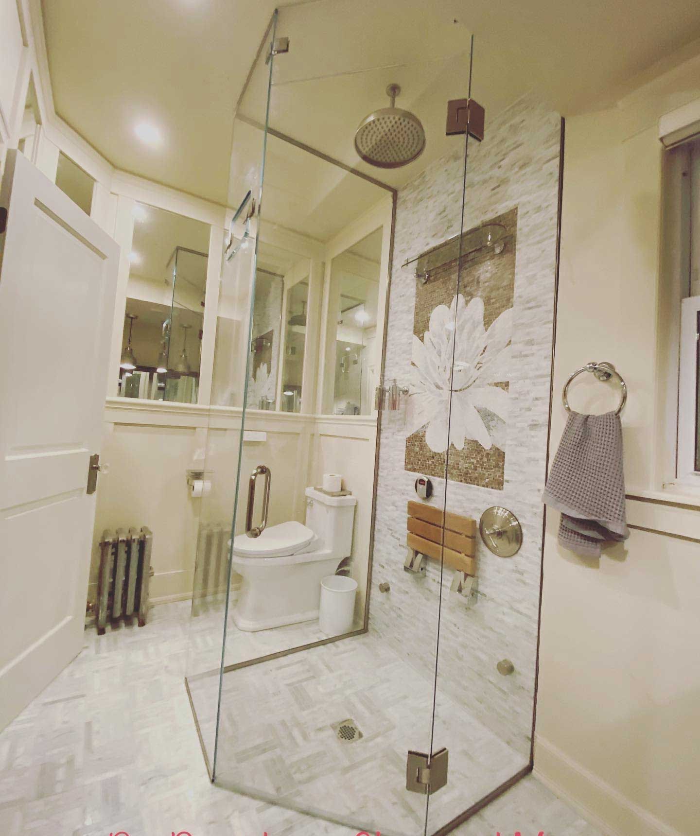 Modern bathroom with glass shower enclosure, mosaic accent wall, and white fixtures.