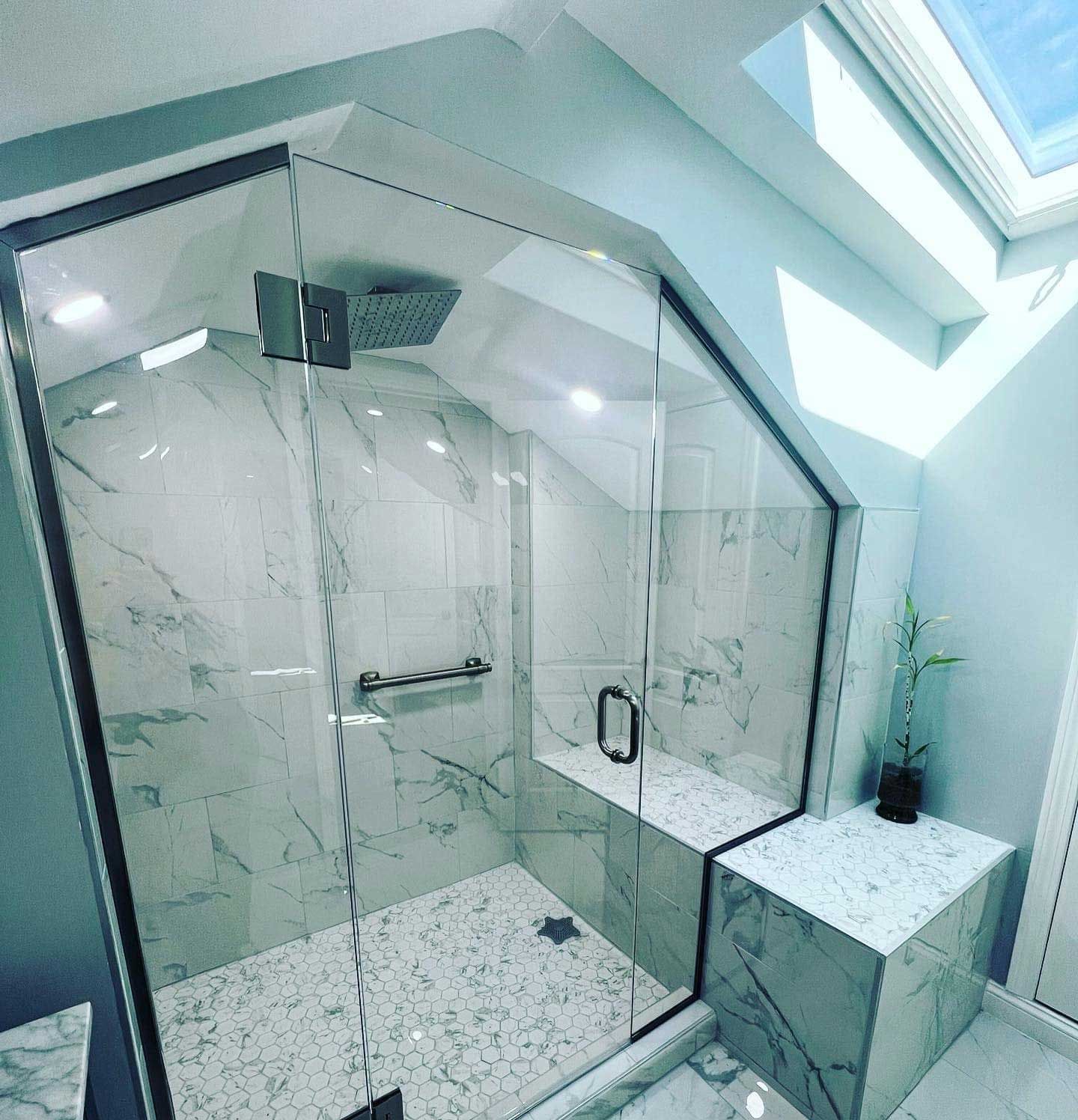 Modern shower with marble tile and glass door under a skylight.
