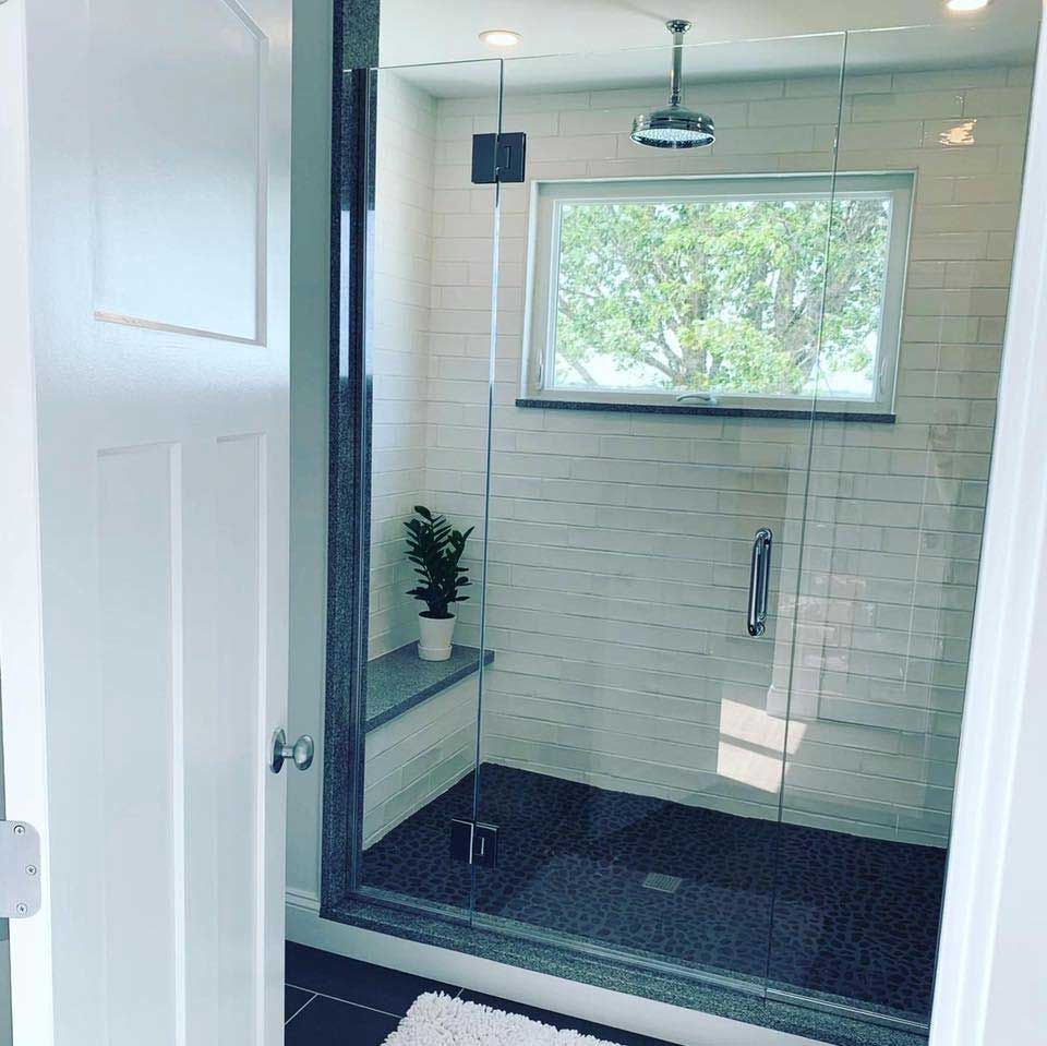 Glass shower with white tile walls, a window, and a gray bench.
