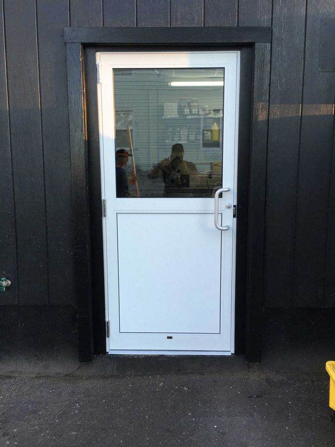 White and glass door set in a black frame, on a dark building exterior.