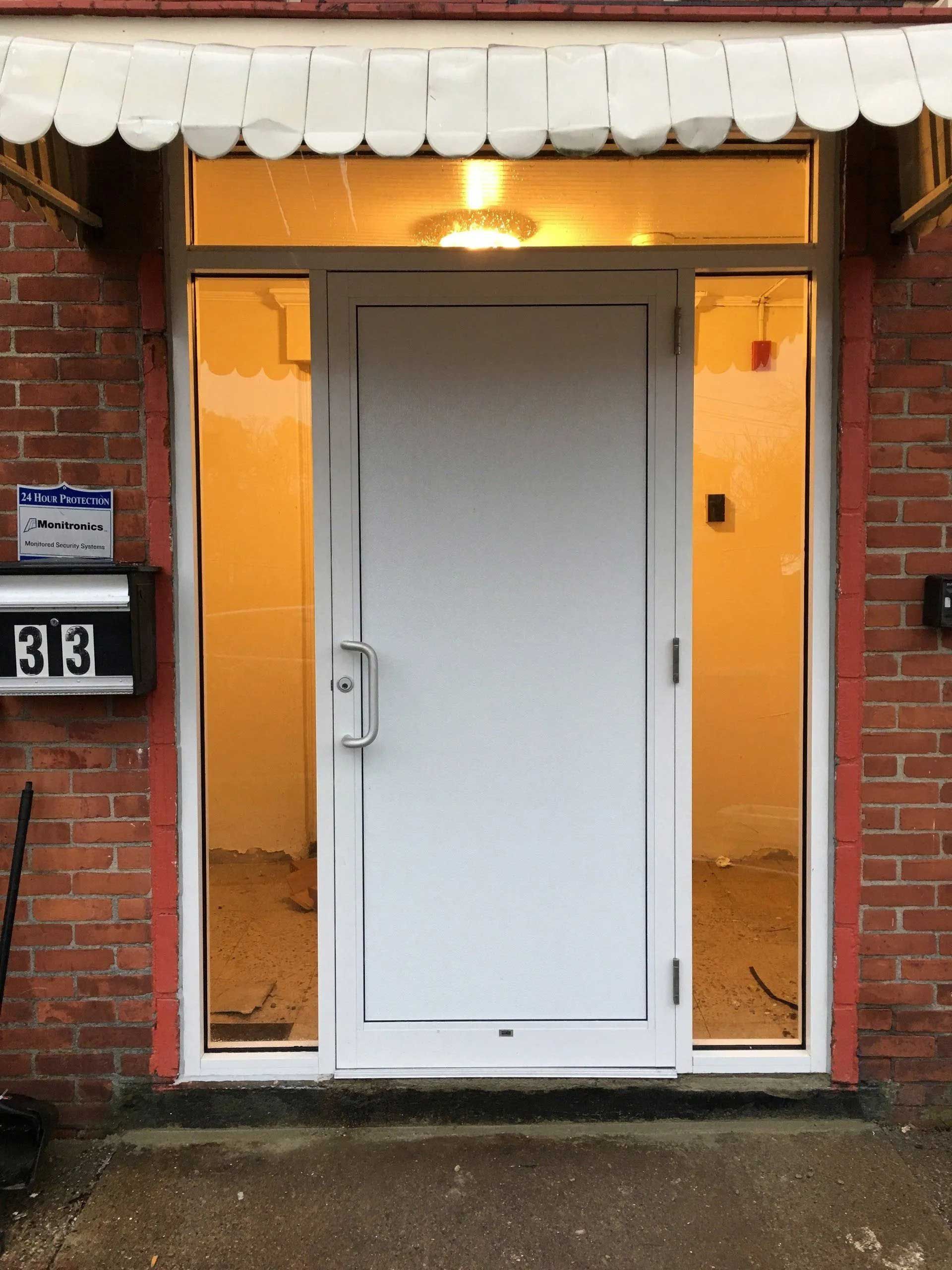 White door with sidelights in a brick building entrance, beneath a white awning. The door has a silver handle.