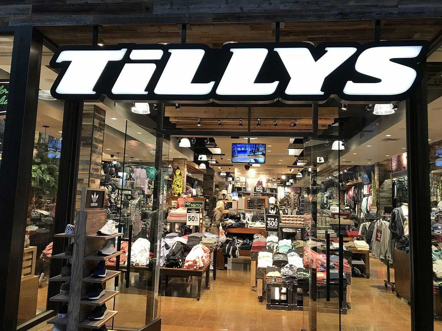 Entrance to a Tillys store with illuminated sign above glass doors, merchandise visible inside.