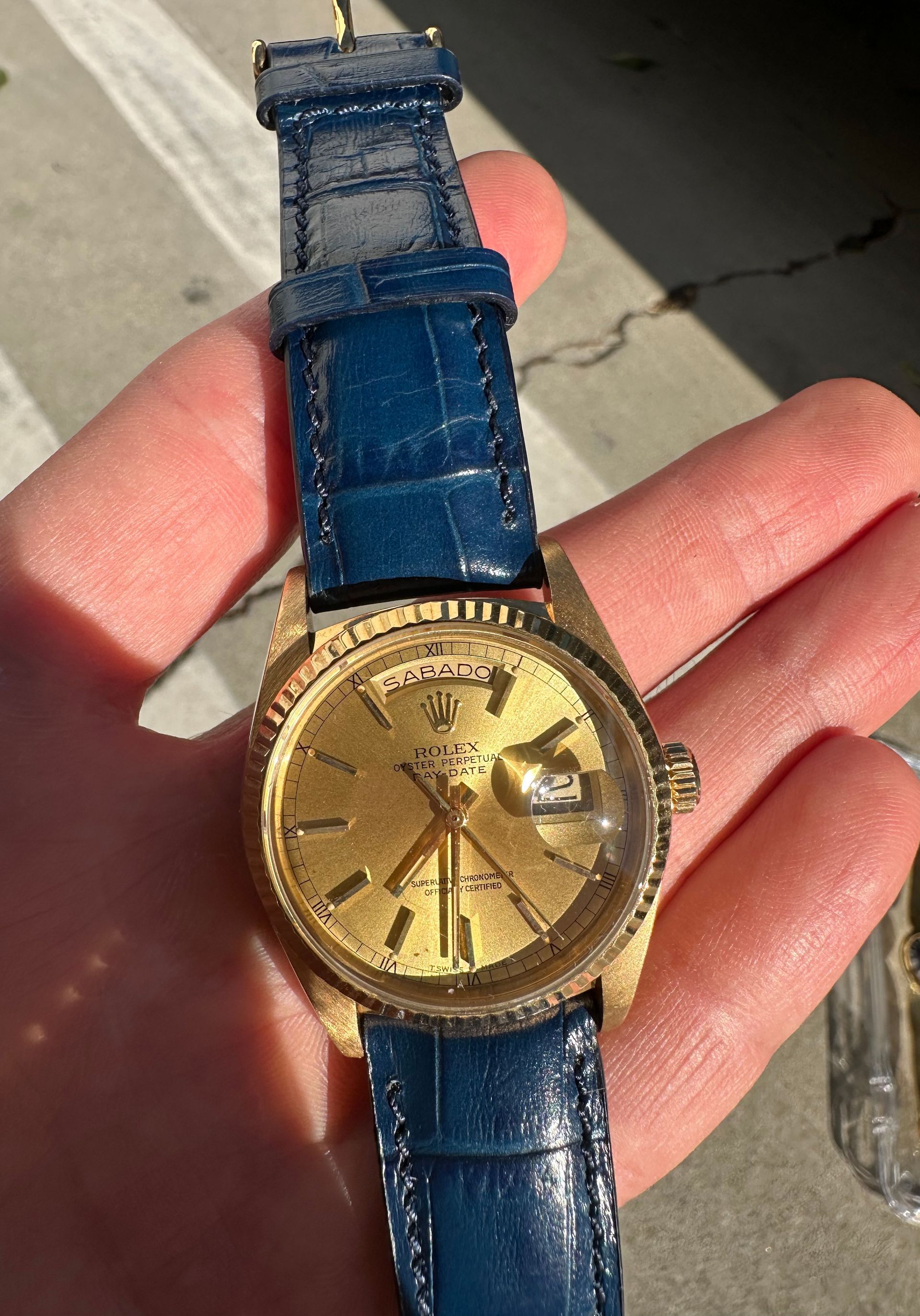 A person is holding a gold watch with a blue band