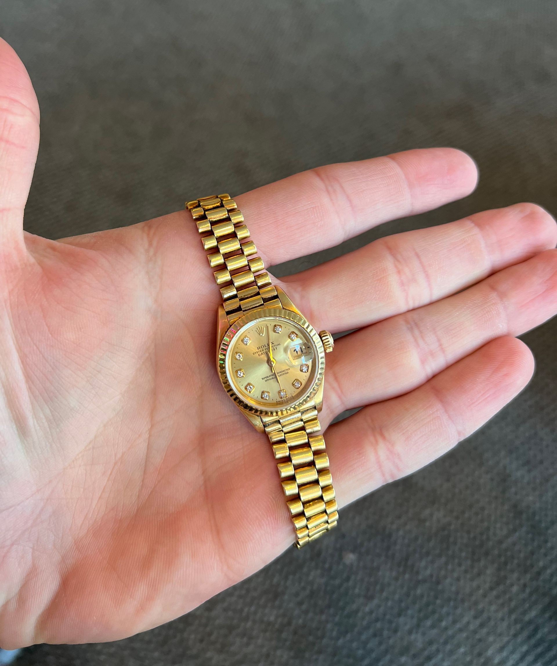 A person is holding a gold watch in their hand