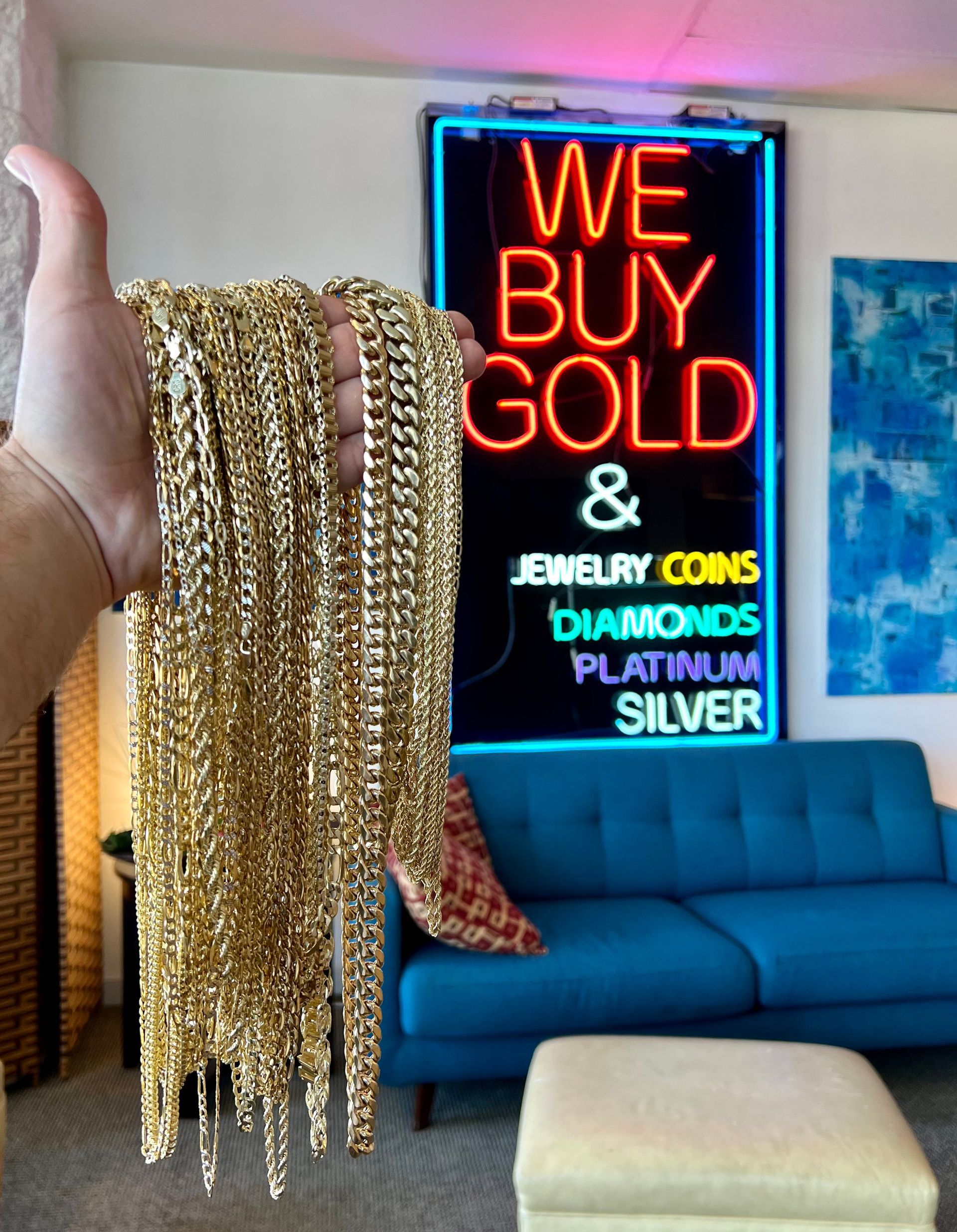 A person is holding a gold chain in front of a neon sign that says we buy gold and jewelry coins