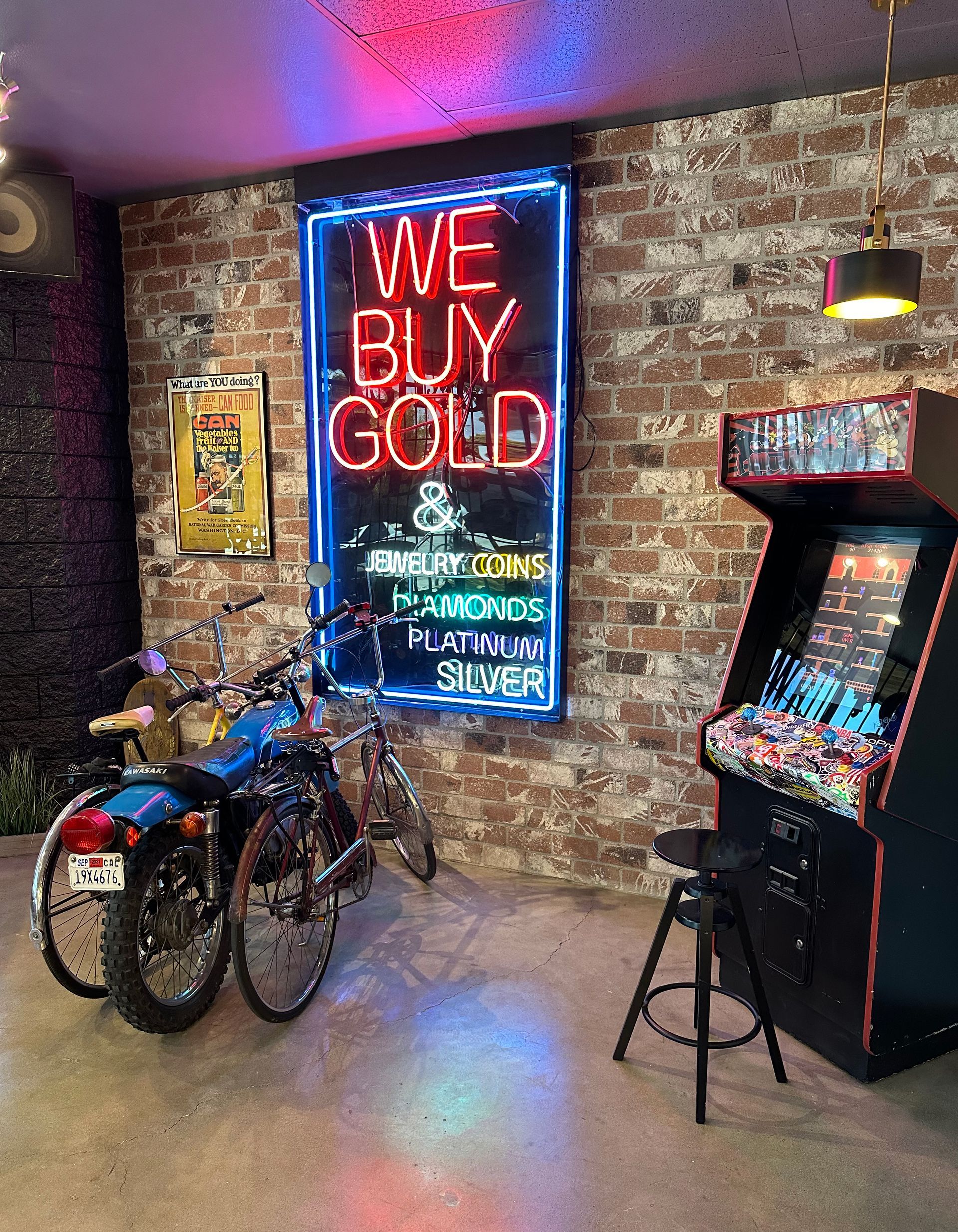 A motorcycle is parked in front of a neon sign that says `` we buy gold ''.