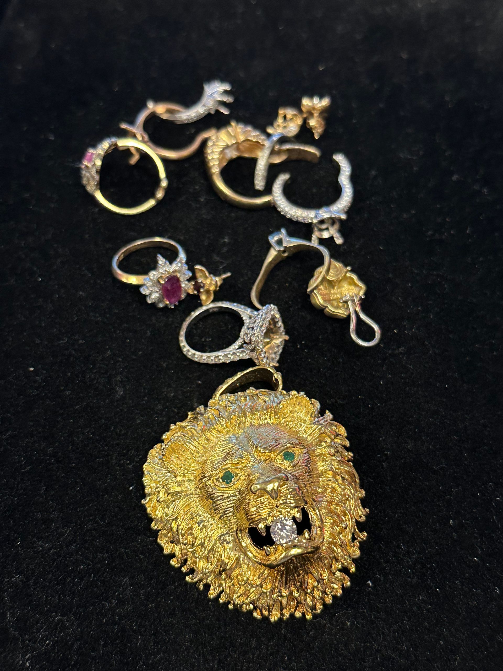 Golden lion pendant and several diamond rings and earrings on a black surface.
