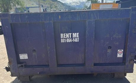 A dumpster is parked in a gravel lot.