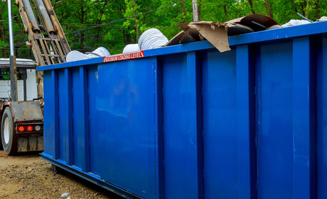 A large blue dumpster is sitting next to a truck.