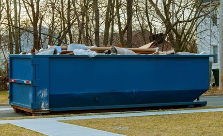 A blue dumpster filled with trash is parked in front of a house.