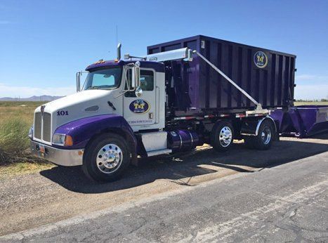 A purple dump truck is parked on the side of the road.