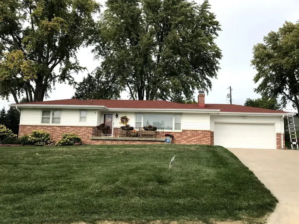 A single-story ranch home with white siding, a reddish-brown brick base, a red roof, and an attached two-car garage.